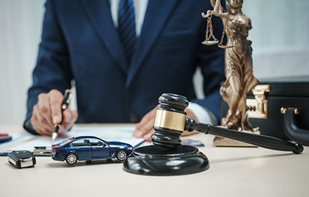 Defense Lawyer With Case Documents, Gavel, Scales of Justice, and Car Figurine on Top of Desk